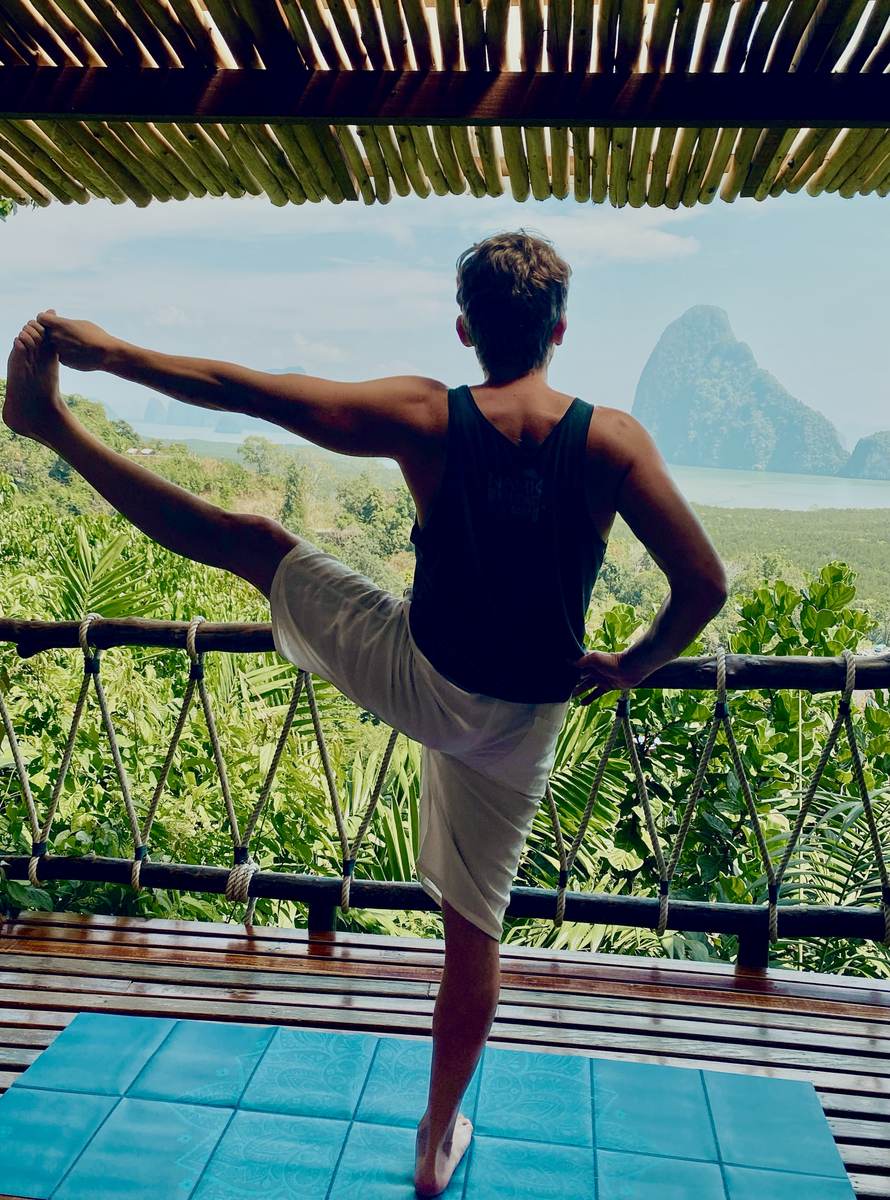Logan practicing yoga overlooking the mountains and water of Thailand